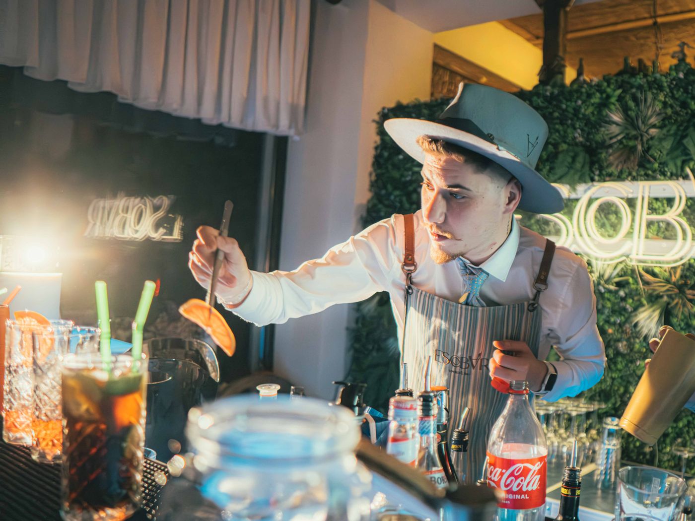 A bartender in a hat and striped apron garnishing a cocktail with an orange slice
